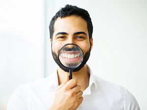 man using magnifying glass to show off his smile with dental crowns in Fayetteville 