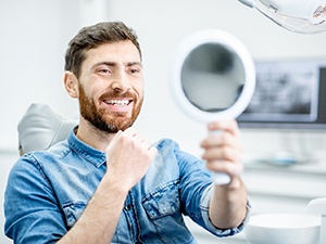 Man with mirror looking at his dental implants in Fayetteville, NY