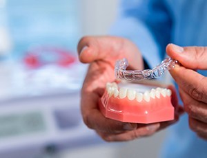 Dentist placing Invisalign aligner on model of teeth