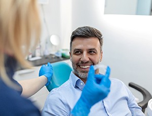 Man smiling at dental assistant holding Invisalign aligner