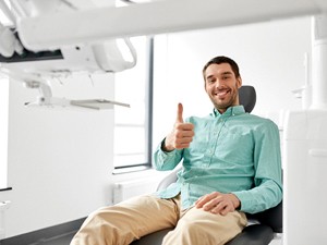 Man with khaki pants smiling in dental chair with thumb up
