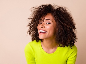 Woman with curly hair and neon shirt smiling with veneers