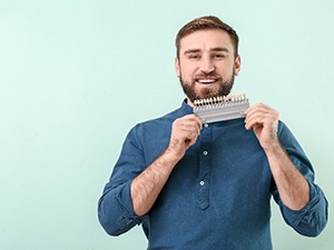 Smiling man in blue shirt holding tooth shade guide