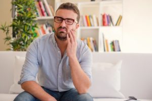 man sitting on couch holding his mouth in pain 