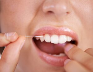 Woman getting stuck food out of her teeth by flossing